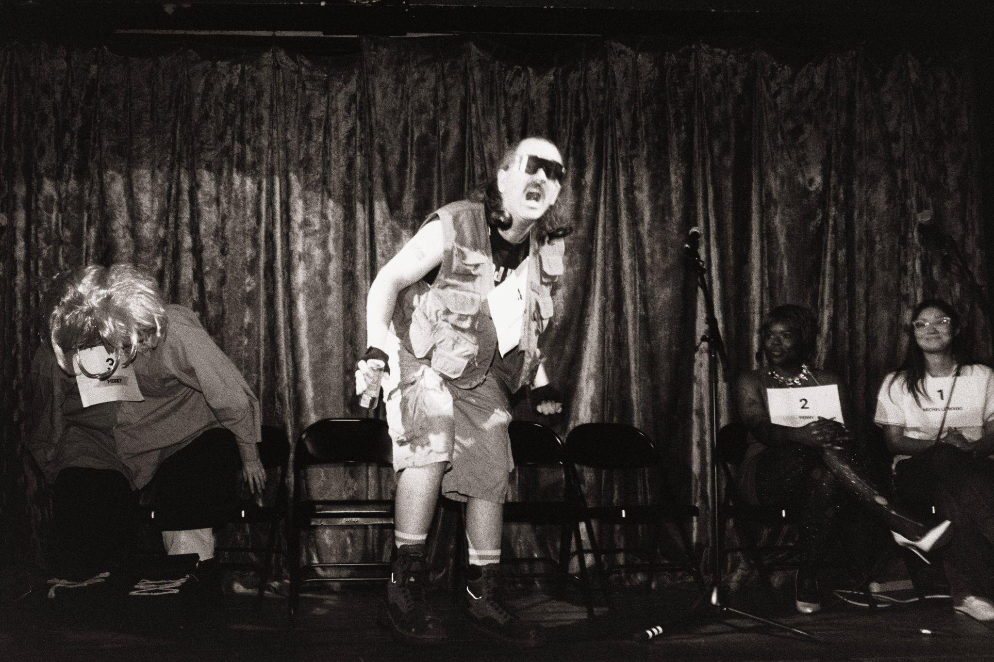 Costumed spelling bee contestants sit onstage while one contestant performs